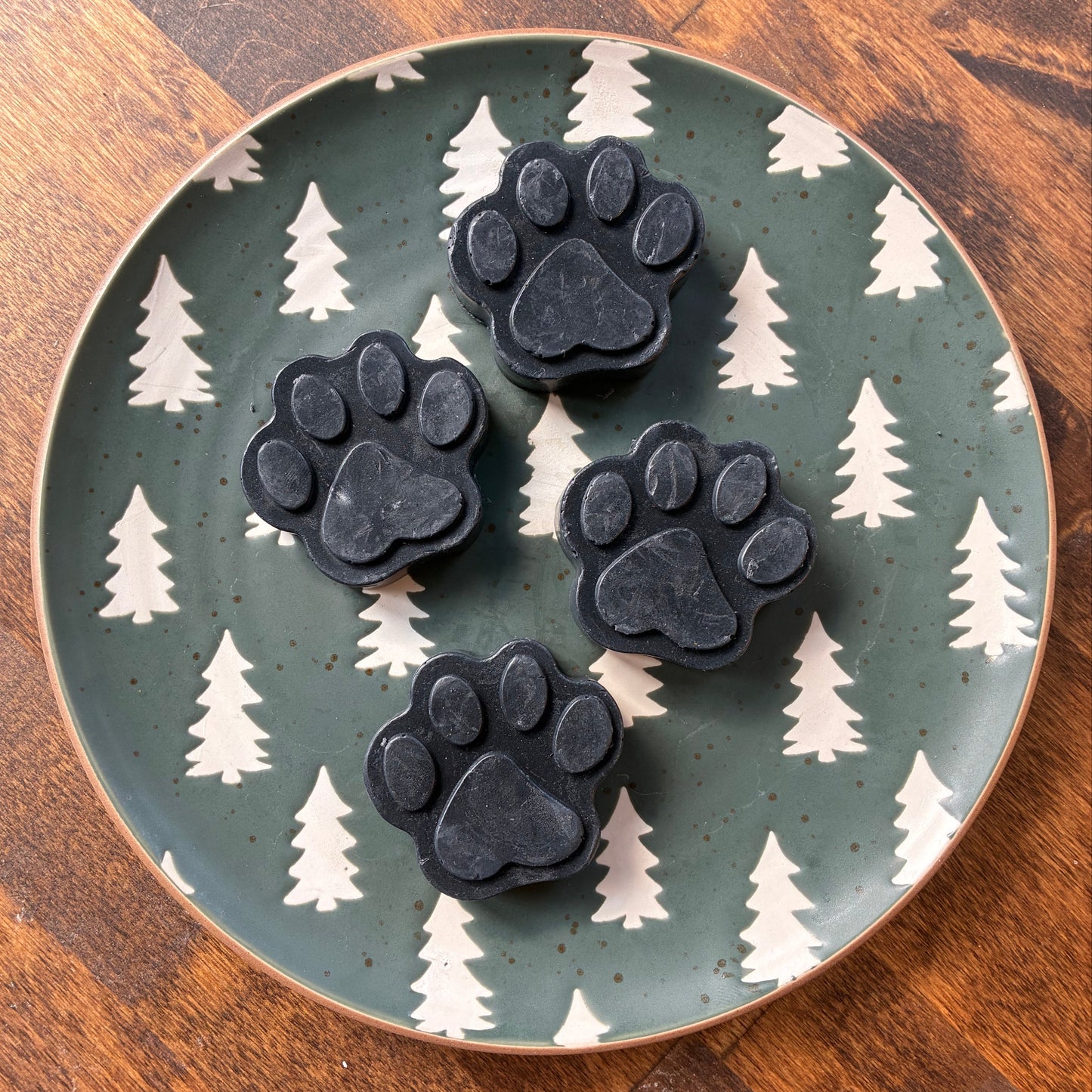 Black paw-shaped objects on a ceramic plate with tree pattern on a wooden surface